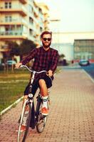 elegant Mens in zonnebril rijden een fiets Aan stad straat foto