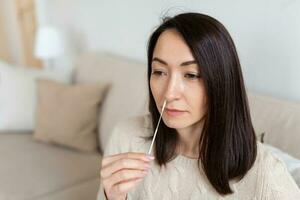 schot van een vrouw gebruik makend van katoen wattenstaafje terwijl aan het doen coronavirus pcr testen. vrouw duurt coronavirus monster van haar neus- Bij huis. vrouw Bij huis gebruik makend van een nasaal wattenstaafje voor covid19. foto