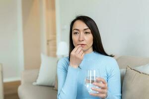 Aziatisch vrouw duurt pil met glas van water in hand. benadrukt vrouw drinken verdoofd antidepressiva medicijnen. vrouw voelt depressief, nemen drugs. geneesmiddelen Bij werk foto