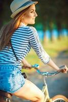 lief jong vrouw in een hoed rijden een fiets in een park foto