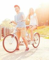 gelukkig paar - Mens en vrouw rijden een fiets in de park buitenshuis foto