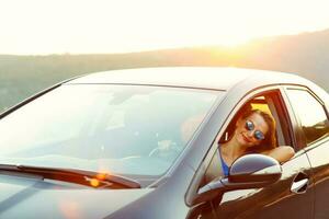 glimlachen vrouw het rijden een auto Bij zonsondergang foto