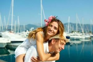 aantrekkelijk jong paar hebben pret in de jachthaven met afgemeerd boten Aan een luxe waterkant in zomer zonneschijn foto