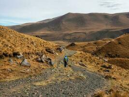 trekking in de Kaukasus berg. Mens met een rugzak is beklimming zwaar Aan een berg pad. avontuur solo op reis levensstijl concept, actief weekend vakantie Aan de wild natuur. foto