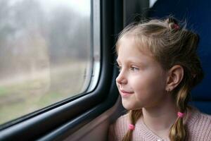 de kind is Aan de trein en looks uit de venster. een weinig meisje reist in een trein. foto