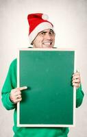 Mens Holding een schoolbord vervelend de kerstman hoed foto