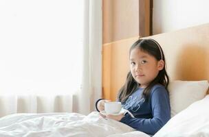 schattig Aziatisch meisje Holding heet melk Aan bed foto