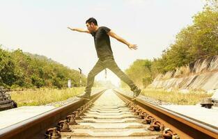 Mens vervelend zwart overhemd verspreidt zijn handen en wandelen Aan trein sporen foto