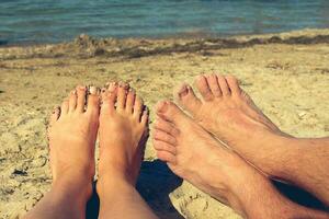 vrouw en mannetje voeten Aan de achtergrond van blauw zee. paar aan het liegen en resting Aan de strand. de concept van een Mens voldoet aan een vrouw - een vakantie romantiek. foto