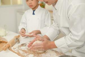 jong Aziatisch vader en zijn zoon vervelend chef uniform bakken samen in keuken Bij huis foto