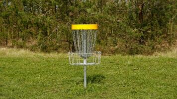 schijf golf mand. frisbee golf is sport en hobbie in buitenshuis park. metaal mand met kettingen voor schijf spel omringd door levendig groen bomen. foto