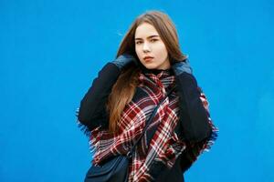 mooi vrouw met een sjaal en jas poseren in de buurt een helder blauw muur foto