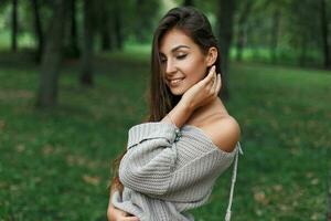 mooi gelukkig jong vrouw glimlachen in een grijs trui in een groen park. foto