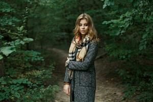 mooi jong vrouw in een gebreid sjaal en herfst jas in de buurt de groen bladeren foto