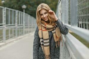 mooi jong meisje met een glimlach in een warm sjaal en jas in herfst dag. foto