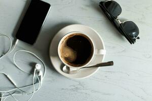 koffie, telefoon met koptelefoon, zonnebril Aan een wit houten tafel. foto