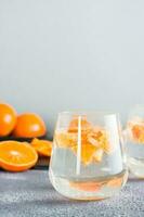 niet alcoholisch cocktail mineraal water met stukken van mandarijnen in een glas en rijp fruit De volgende naar Aan de tafel. ontgiften voedsel. kopiëren ruimte. verticaal visie foto