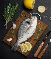 rauw geheel dorado vis Aan houten keuken bord en specerijen voor Koken, top visie Aan zwart tafel foto