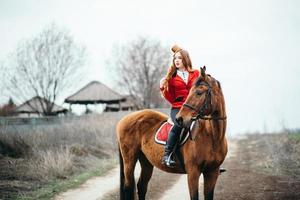 roodharig jockeymeisje in een rood vest en zwarte hoge laarzen met een paard foto