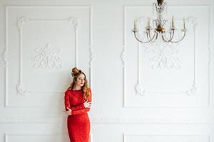 jong meisje met rood haar in een felrode jurk in een lichte kamer foto