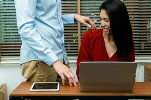 baas aanraken schouder van een jong vrouw werknemer in kantoor Bij werkplek. ze is ongemakkelijk en bang van seksueel ongepast misbruik van een collega. concept van seksueel Intimidatie in de werkplaats foto