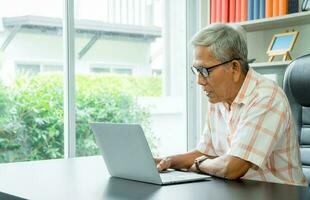 gelukkig senior Aziatisch gebruik makend van de laptop voor berekenen en maken een Notitie van dagelijks uitgaven. concept van levensstijl, aan het leren, en financiën bedrijf foto