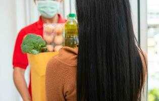 Aziatisch levering Mens van supermarkt vervelend een gezicht masker en Holding een zak van vers voedsel, groenten, en fruit voor geven naar klanten Bij huis. concept van uitdrukken kruidenier onderhoud en nieuw levensstijl foto