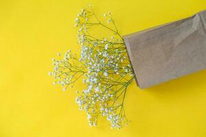 een boeket van klein gypsophila bloemen in een eco zak Aan een geel tafel achtergrond met ruimte voor tekst foto