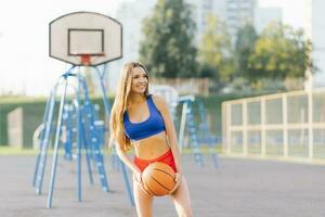 een atletisch jong vrouw in sport- shorts en t-shirts Toneelstukken Aan een basketbal rechtbank met een bal foto