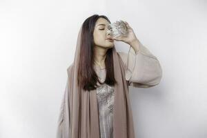 blij Aziatisch moslim vrouw vervelend hoofddoek is drinken een glas van water, geïsoleerd Aan wit achtergrond. foto