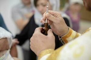 de priester handen zijn Holding een fles van wierook en een borstel voor doop. foto