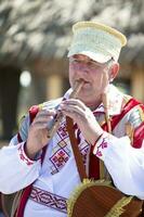 08 29 2020 Wit-Rusland, lyaskovichi. viering in de stad. een ouderen Slavisch Mens in nationaal jurk Toneelstukken de pijp. foto