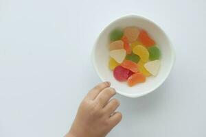 kind hand- plukken kleurrijk snoep zoet gelei in een kom Aan tafel foto