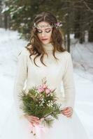 mooi bruid in een wit jurk met een boeket in een met sneeuw bedekt winter Woud. portret van de bruid in natuur. foto