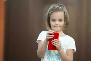 weinig mooi meisje Holding een mobiel telefoon en op zoek Bij de camera. foto