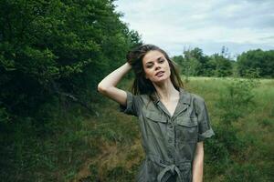 vrouw Aan natuur een vrouw in een groen jumpsuit houdt haar haar- op zoek vooruit vers lucht reizen foto