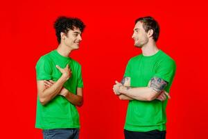 twee vrienden in groen t-shirts zijn staand kant door kant communicatie positief rood achtergrond foto