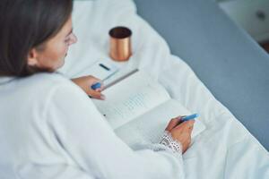 brunette vrouw Aan slecht met kladblok of boek foto