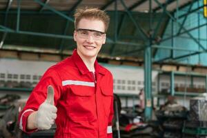 portret van een jong auto monteur tonen duimen omhoog in reparatie garage, auto reparatie en onderhoud concepten foto