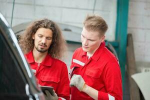 mechanica in uniform met tablets werken in auto onderhoud, jong Kaukasisch auto mechanica met een controlelijst, technicus controle modern auto's in garage, auto reparatie, en onderhoud concepten foto