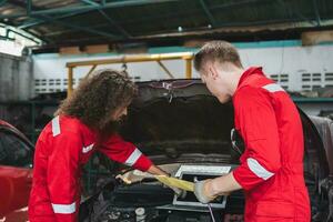 jong Kaukasisch auto monteur met een controlelijst, mechanica in uniform zijn werken in auto onderhoud, technicus controle modern auto Bij garage, auto reparatie en onderhoud concepten foto