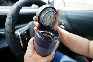 Aziatisch vrouw bestuurder houden thermo mok met heet koffie in auto, gevaarlijk en risico een ongeluk. foto