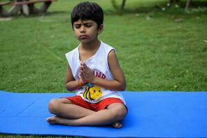 Aziatisch slim kind aan het doen yoga houding in de maatschappij park buitenshuis, kinderen yoga houding. de weinig jongen aan het doen yoga en meditatie oefening. foto