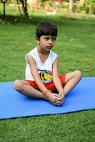 Aziatisch slim kind aan het doen yoga houding in de maatschappij park buitenshuis, kinderen yoga houding. de weinig jongen aan het doen yoga en meditatie oefening. foto