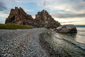 visie van de kiezelsteen kust naar de rots sjamanka van de eiland van olkhon Aan meer Baikal. foto