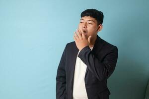 portret van jong Aziatisch bedrijf Mens in gewoontjes pak geeuwen in verveeld uitdrukkingen. geïsoleerd beeld Aan blauw achtergrond foto
