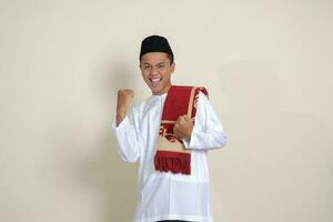 portret van aantrekkelijk Aziatisch moslim Mens in wit overhemd verhogen zijn vuist, vieren succes. geïsoleerd beeld Aan grijs achtergrond foto