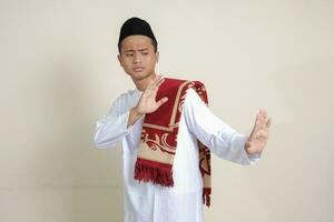 portret van aantrekkelijk Aziatisch moslim Mens in wit overhemd met kalotje vormen een hand- gebaar naar vermijden iets of slecht dingen. geïsoleerd beeld Aan grijs achtergrond foto