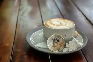 een kop van cappuccino met bitcoin Aan houten tafel Bij cafe. cryptogeld handel concept foto