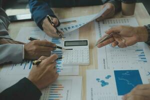 groep van zelfverzekerd bedrijf mensen punt naar grafieken en grafieken naar analyseren markt gegevens, balans vel, account, netto winst naar plan nieuw verkoop strategieën naar toenemen productie capaciteit. foto